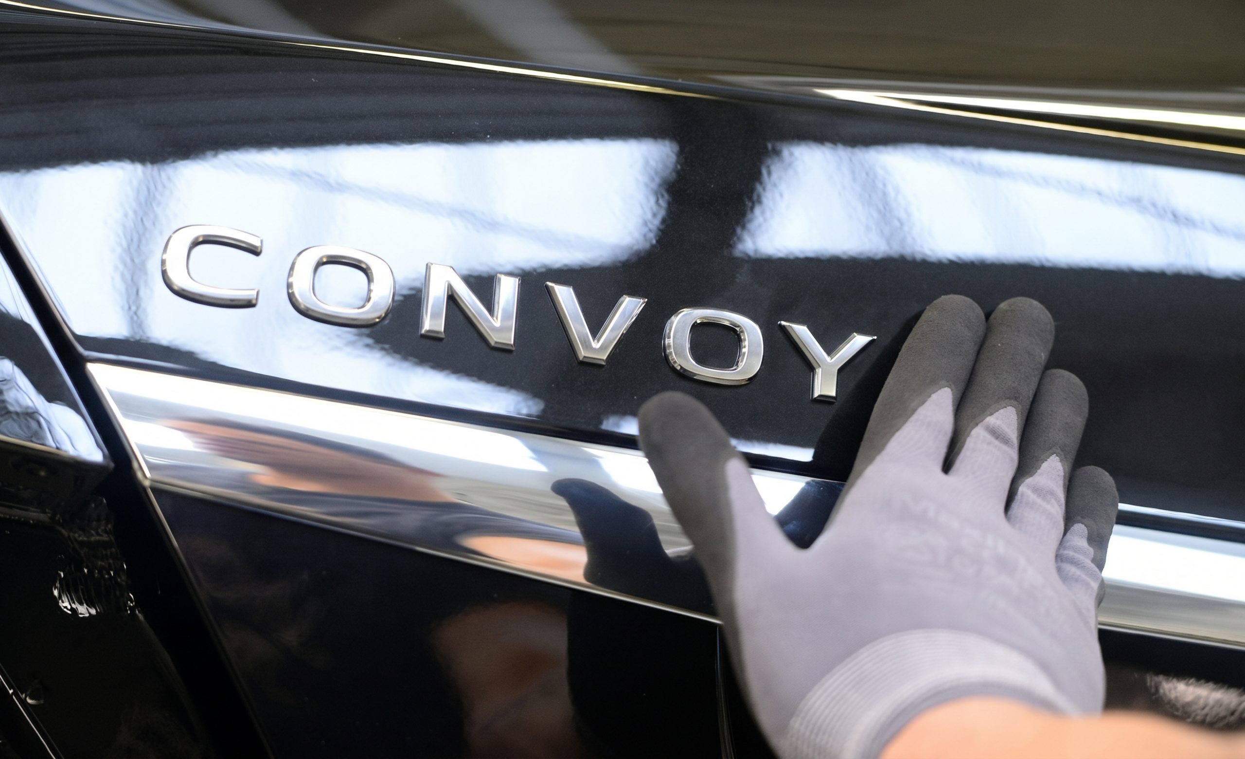 A gloved hand fitting a chrome CONVOY badge to the black paintwork of a car